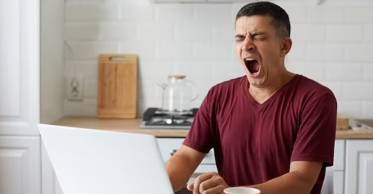  Man standing in Kitchen yawning while looking at laptop 