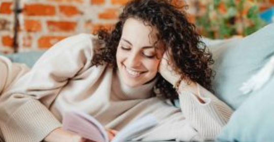 A female smiling while laying down reading a book